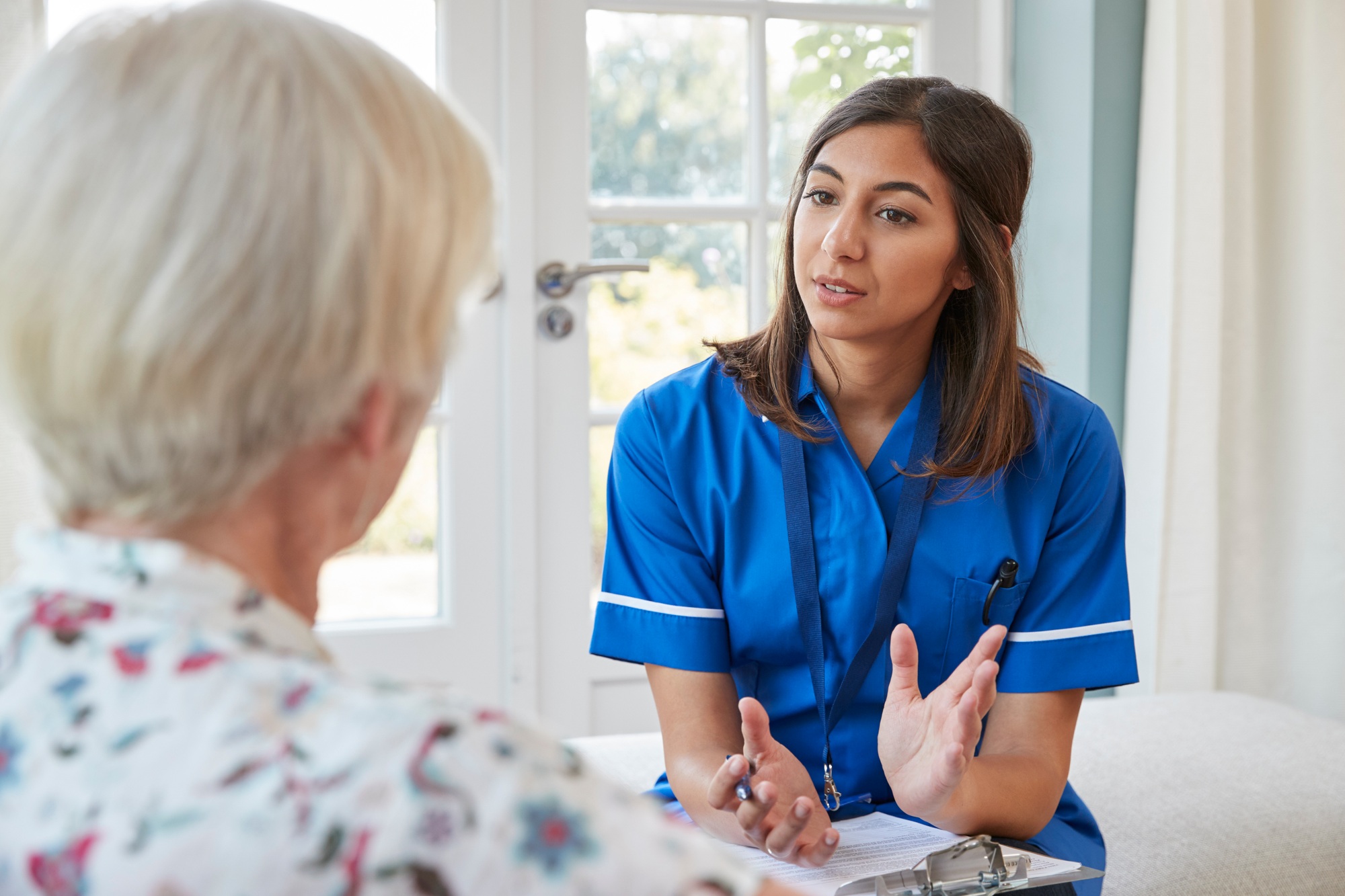 Senior woman talking to young care nurse on home visit